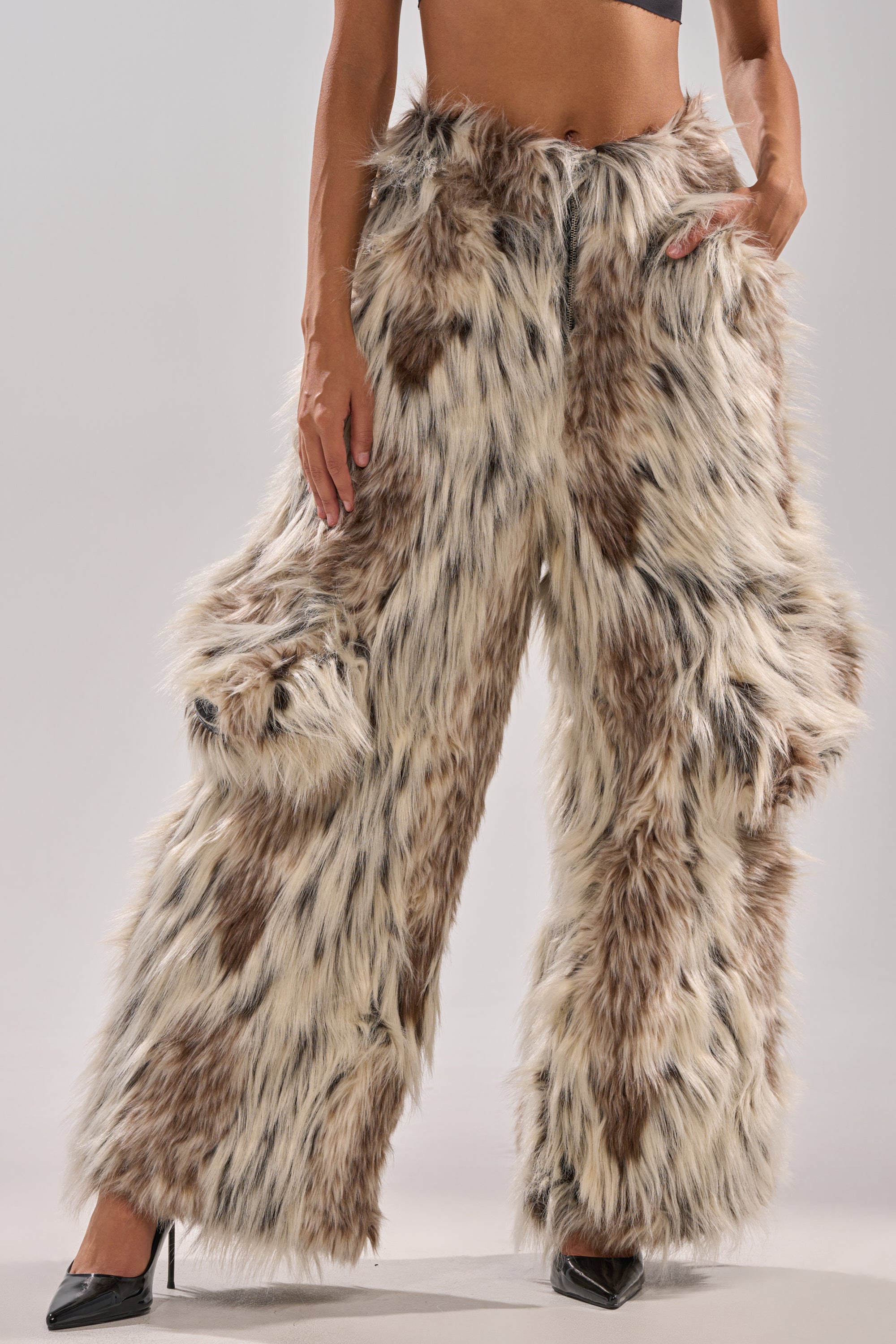Rocking the PARTICULAR TASTE FAUX FUR CARGO PANTS—high-rise, wide-legged, in a brown, black, and white spotted pattern—paired with black heels and a crop top. Only the lower torso and legs are shown for a winter-chic vibe.