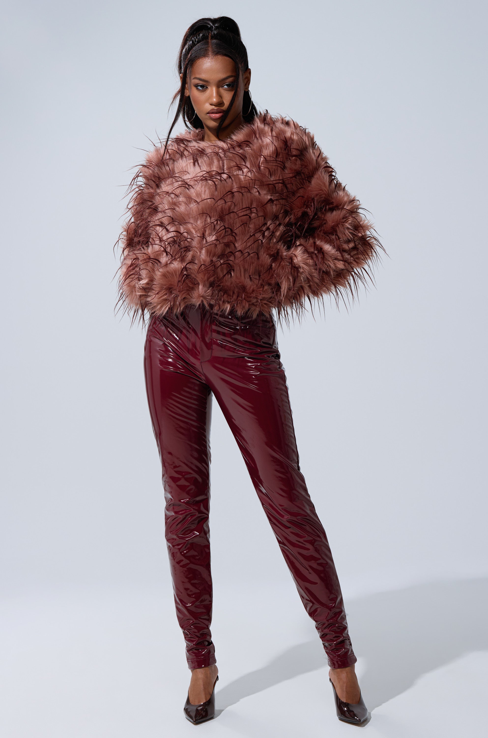 A woman poses confidently in a fluffy, brownish-pink faux fur jacket and ON FIRE FAUX LEATHER LEGGING with matching pointed heels, set against a plain light gray background.