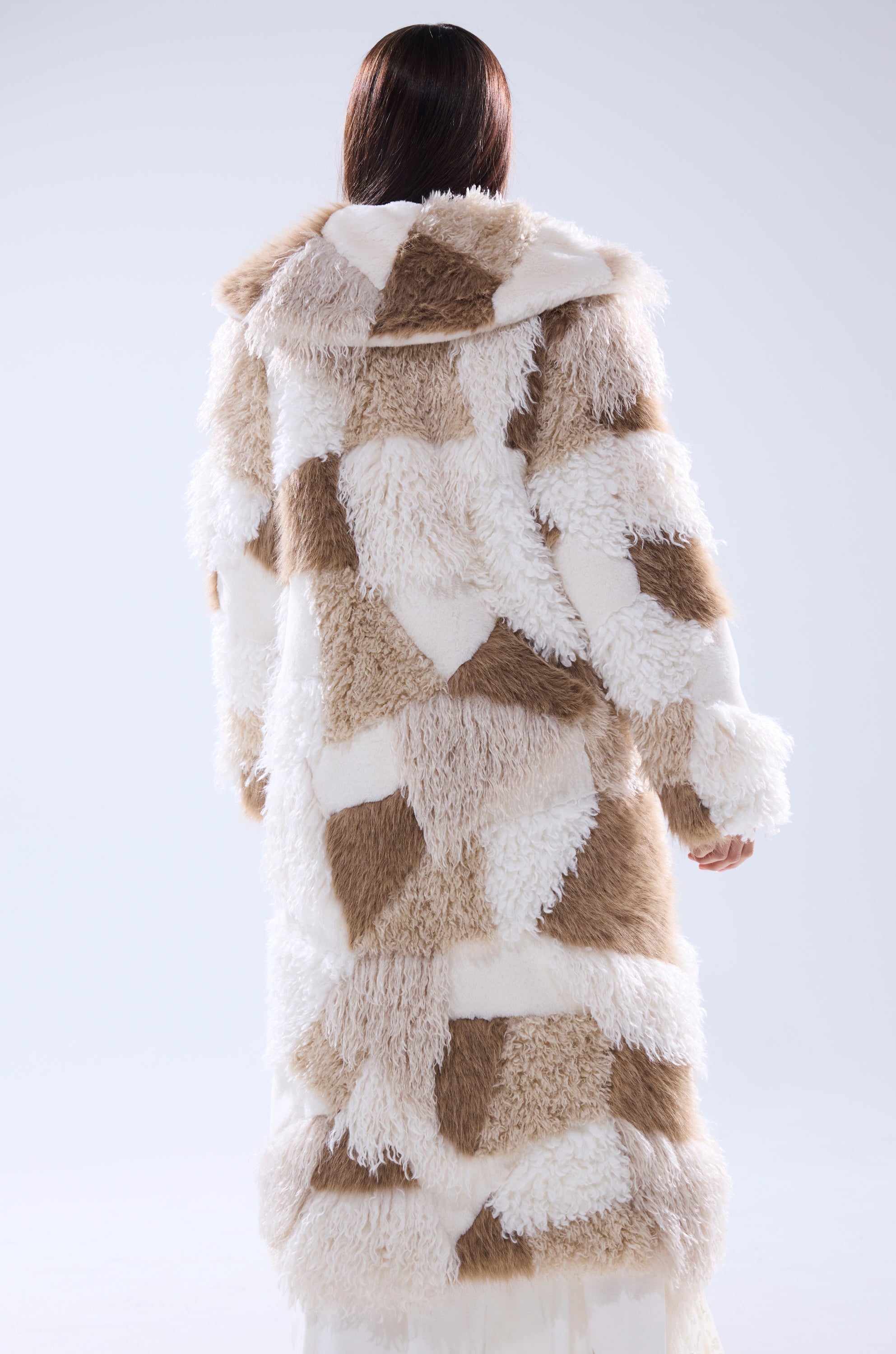 A person with long brown hair stands with their back to the camera against a white background, wearing the IN MY FEELS PATCHWORK FAUX FUR COAT in cream and tan.