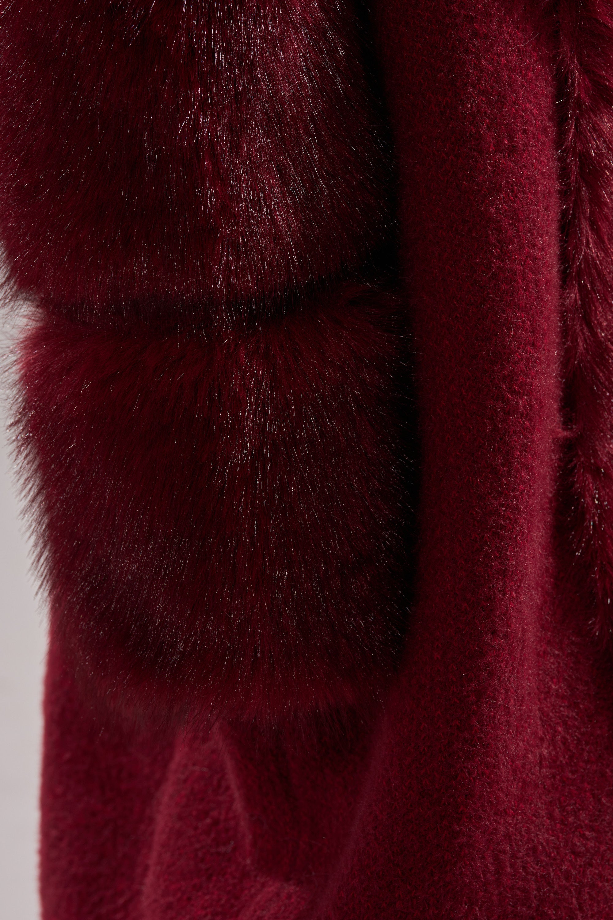 Close-up of the LUXE LIFE FUR CARDIGAN IN BURGUNDY, a deep burgundy knit with two thick, fluffy faux fur bands for a luxurious and elegant look.