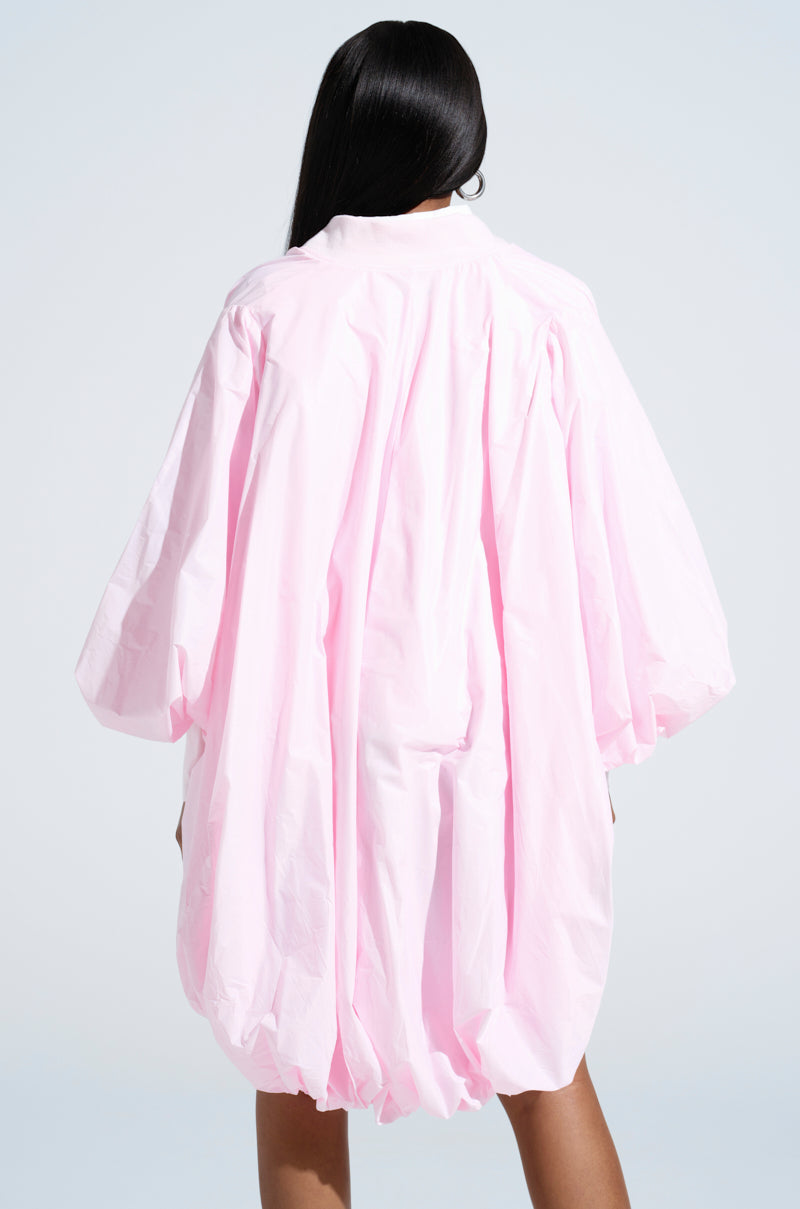 A person with long, straight black hair is seen from the back, wearing the FLOATING NYLON BUBBLE BOMBER IN LIGHT PINK, featuring a loose silhouette with billowy sleeves and a gathered hem, set against a plain light background.