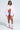 A woman exudes confidence in a white cropped shirt, distressed denim shorts, FLOATING NYLON BUBBLE BOMBER IN LIGHT PINK, pink-and-white high sneakers, white socks, and clear glasses, channeling bold streetwear against a plain light backdrop.