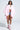 A woman exudes confidence in glasses, a white cropped shirt, denim shorts, and pink high-top sneakers with white socks, layering the FLOATING NYLON BUBBLE BOMBER IN LIGHT PINK for a trendy streetwear look against a light grey background.