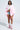 A woman exudes confidence in glasses, a white knotted shirt, denim shorts, white socks, pink high-top sneakers, and the FLOATING NYLON BUBBLE BOMBER IN LIGHT PINK—showcasing bold streetwear style against a plain light background.