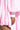 A close-up of a medium-brown hand resting against a leg, partially covered by the FLOATING NYLON BUBBLE BOMBER IN LIGHT PINK. The voluminous bubble silhouette and softly lit background highlight modern streetwear style.