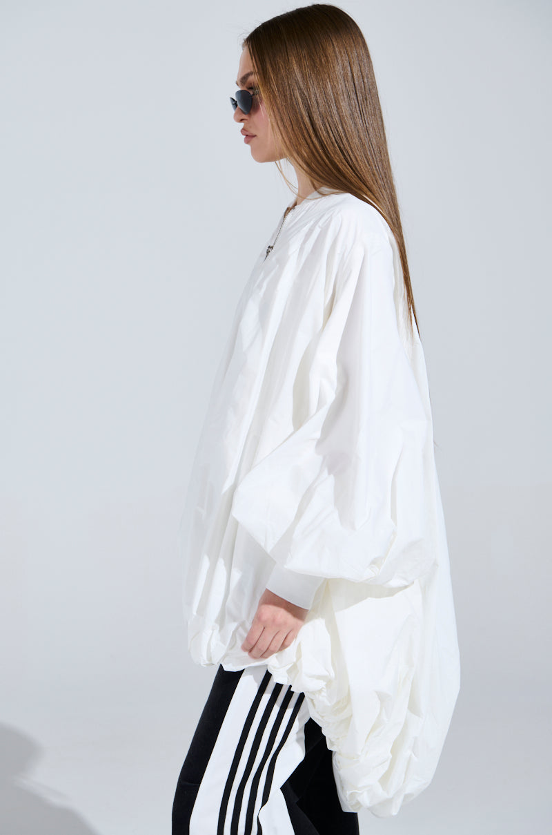 A person in profile wears a FLOATING NYLON BUBBLE BOMBER and dark track pants with white stripes, paired with sunglasses. Their long, straight hair flows against a light gray background.