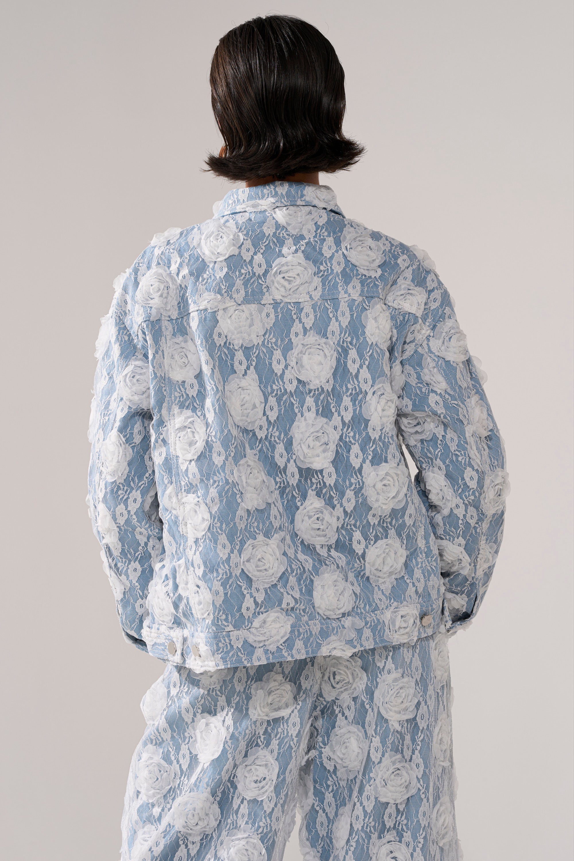 Person with short, dark hair seen from the back, wearing the FOLLOW MY LEAD APPLIQUE DENIM JACKET against a plain, light background.