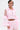 A person wears the ultra-kawaii CANDY LACE TRIM WINDBREAKER in light pink with sheer ruffled sleeves, white lace trim, and bow details. They have short dark hair, hoop earrings, a torso tattoo, and stand against a plain white background.