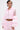 A person with short dark hair, hoop earrings, and torso tattoos wears the CANDY LACE TRIM WINDBREAKER—a light pink, cropped AKIRA jacket with ruffled sleeves and matching shorts.