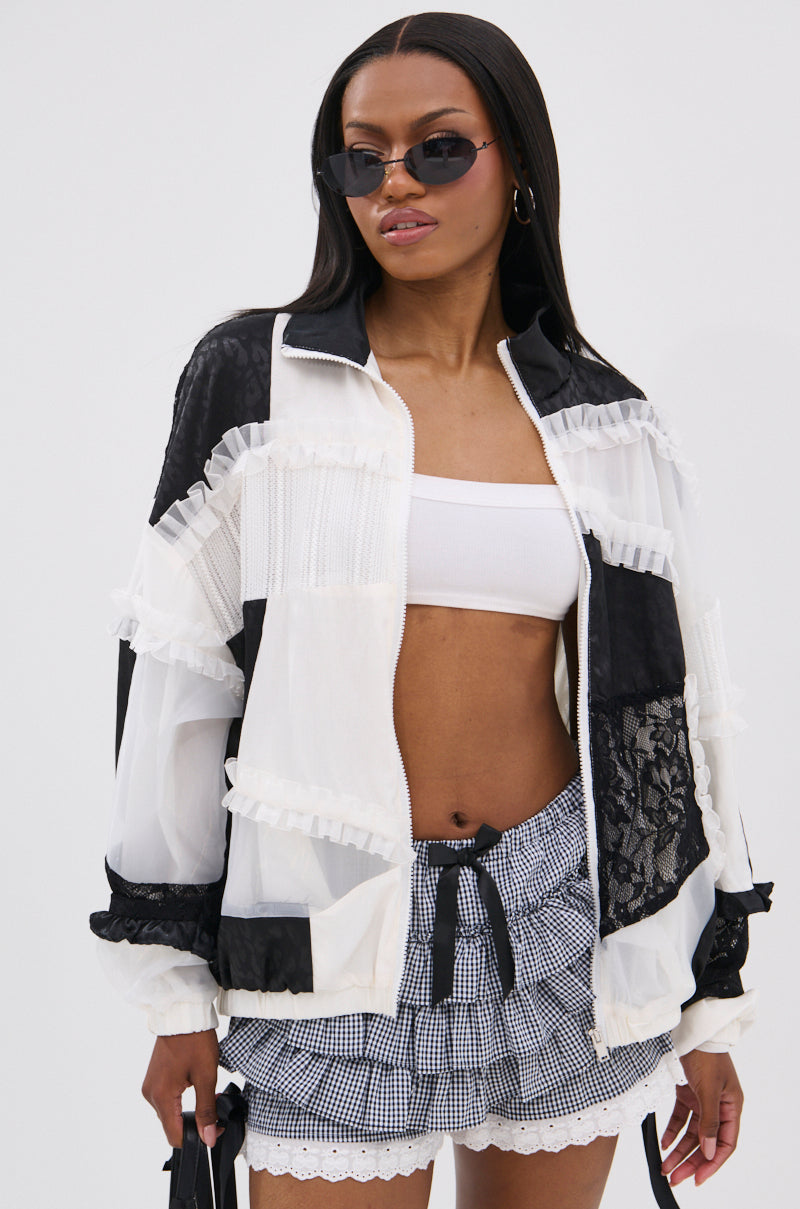 A woman in black sunglasses, a white crop top, and high-waisted gingham shorts stands against a light backdrop, modeling the BLACK DAHLIA PATCHWORK BOMBER with lace details.