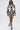 A woman shows off streetwear style in the PAINT THE ROSES RED JACQUARD BOMBER jacket with matching shorts, a black bralette, lace-up boots, sunglasses, and a chain necklace as she walks confidently against a white background.