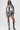 Wearing the PAINT THE ROSES RED JACQUARD BOMBER, matching shorts, a black bralette, sunglasses, necklace, and knee-high black boots with white laces, she radiates bold streetwear style against a plain white background.