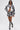 A woman in sunglasses rocks the PAINT THE ROSES RED JACQUARD BOMBER, paired with floral shorts, a black bralette, and black heeled boots with white laces as she walks confidently against a white background.