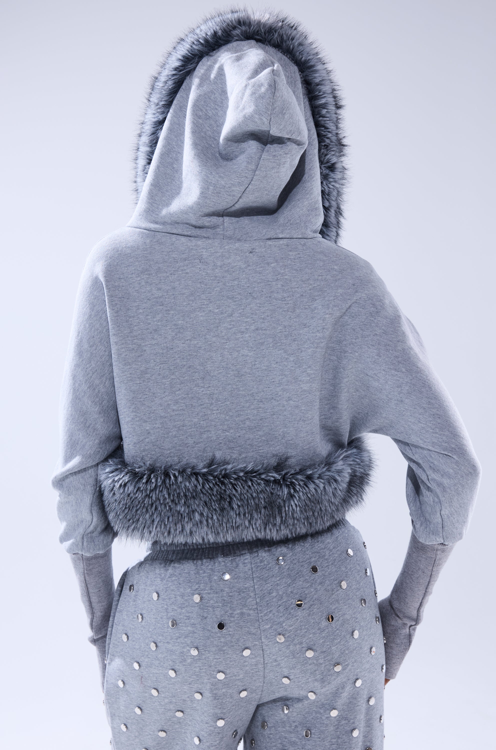 A person shown from the back wears the MOVIN DIFFERENT SWEATSHIRT WITH FUR TRIM and matching gray pants with metallic studs. 6