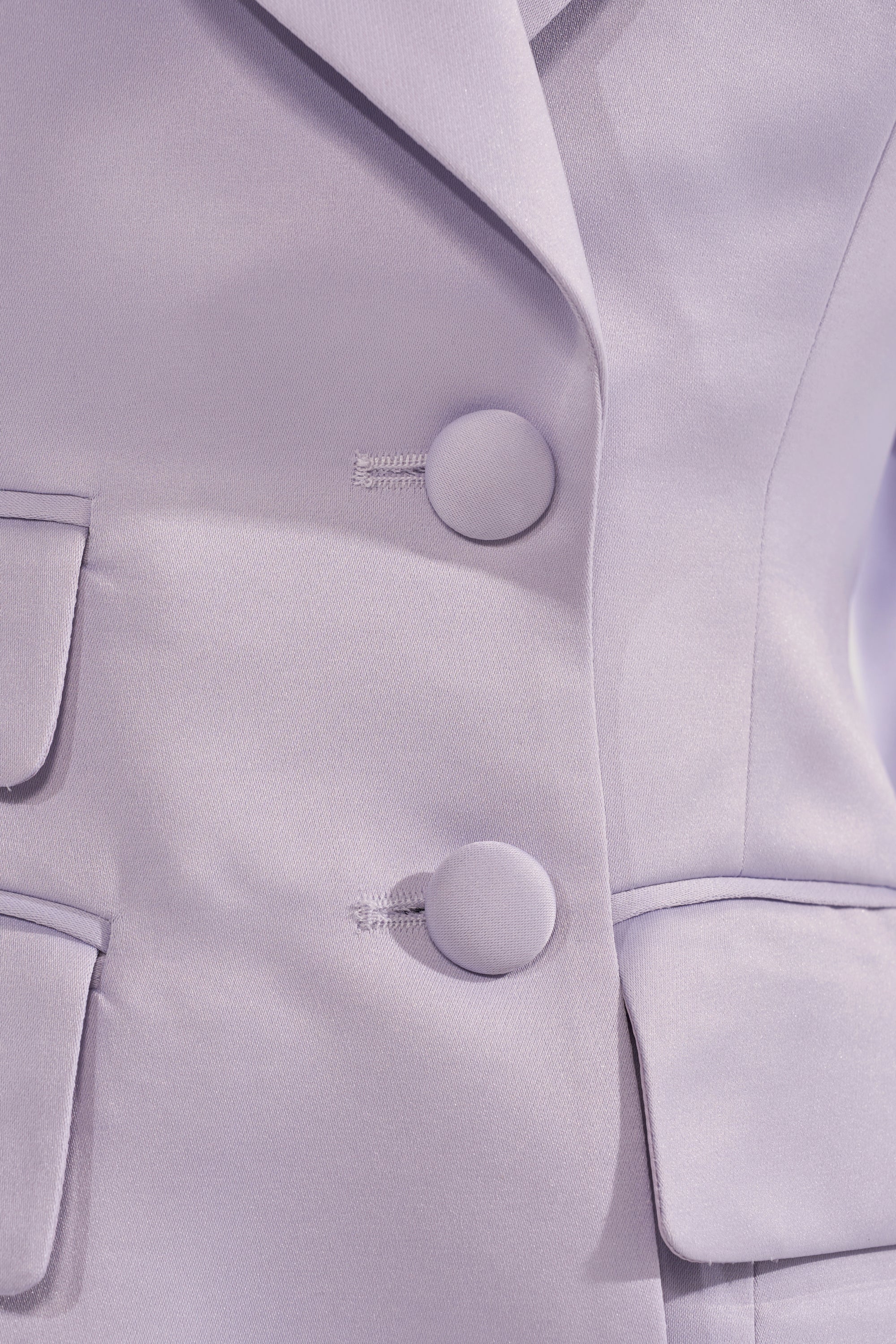 Close-up of the PERFECT FIT BLAZER IN LILAC for women, displaying two fabric-covered buttons and flap pockets that emphasize its smooth texture, tailored seams, and elegant longline design. 9