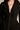 A person wearing the fitted black CORTEZ PEPLUM BLAZER with metallic zippered cuffs and layered silver necklaces featuring black and silver cross pendants, focusing on the jewelry and upper body.