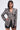 A woman wears the PUSH TO START LACE BLAZER, featuring a tailored silhouette, bold shoulders, and large pearl buttons, paired with black shorts. She has straight dark hair, hoop earrings, and stands against a plain light background.