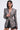 A woman with straight dark hair poses confidently in the PUSH TO START LACE BLAZER—a long, fitted black lace blazer with puffed shoulders, deep V-neck, side cutouts, and black shorts—against a light background.