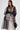 A woman wears the CAN I KICK IT ORGANZA TRENCH with puff sleeves and a wide belt over a white lace top and pants, holding a black handbag. The A-line silhouette pops against the plain, light-colored background as she looks downward.