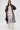 A woman stands against a white background wearing the CAN I KICK IT ORGANZA TRENCH over a strapless white lace top and matching pants. She carries a black handbag and finishes the look with gold hoop earrings.