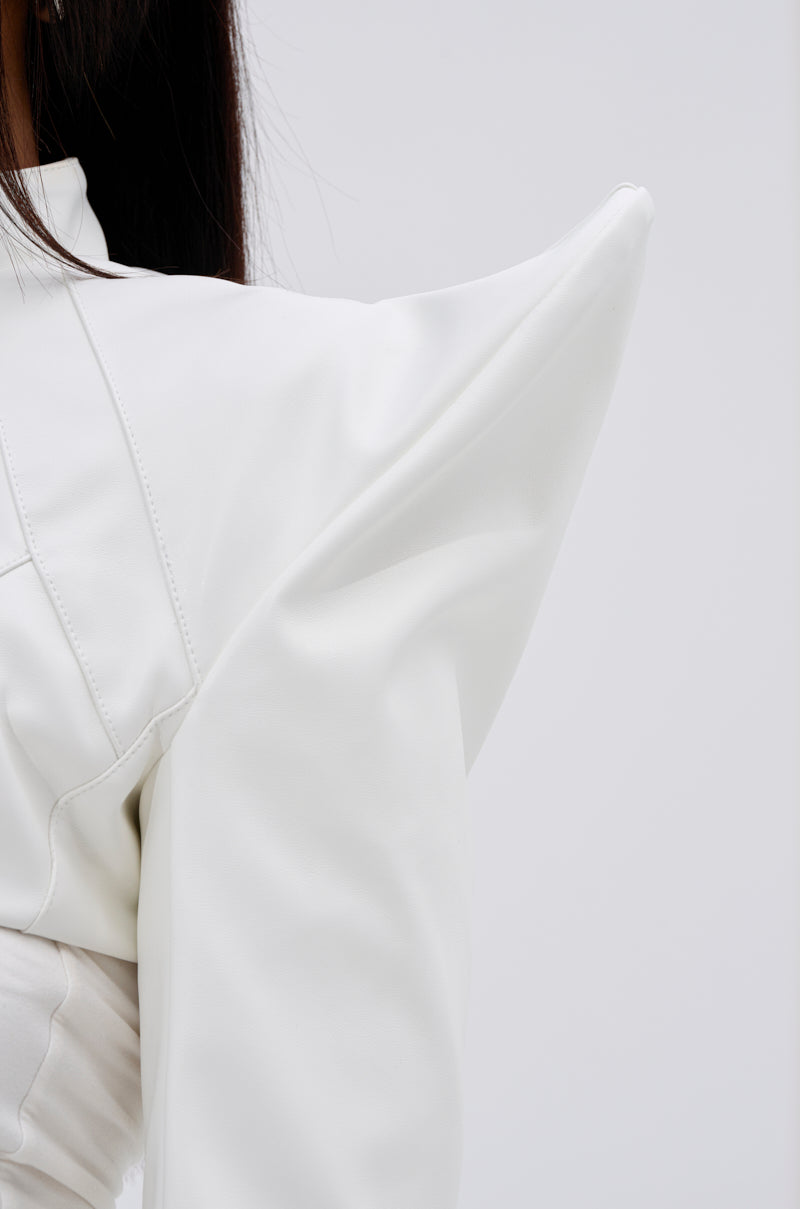 Close-up of a person wearing the TAKING NAMES MOTO BOLERO, featuring an architectural design with exaggerated pointed shoulders, against a plain light gray background. Only part of their upper body and hair is shown. 10