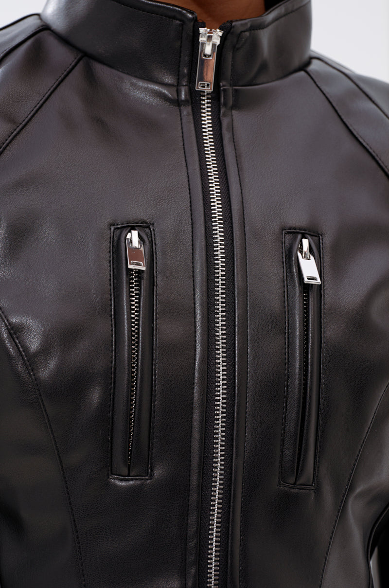Close-up of the STRAIGHT TO THE POINT MOTO jacket—a shiny black faux leather moto with two vertical zippered chest pockets and a central silver zipper, modeled on someone with brown skin.