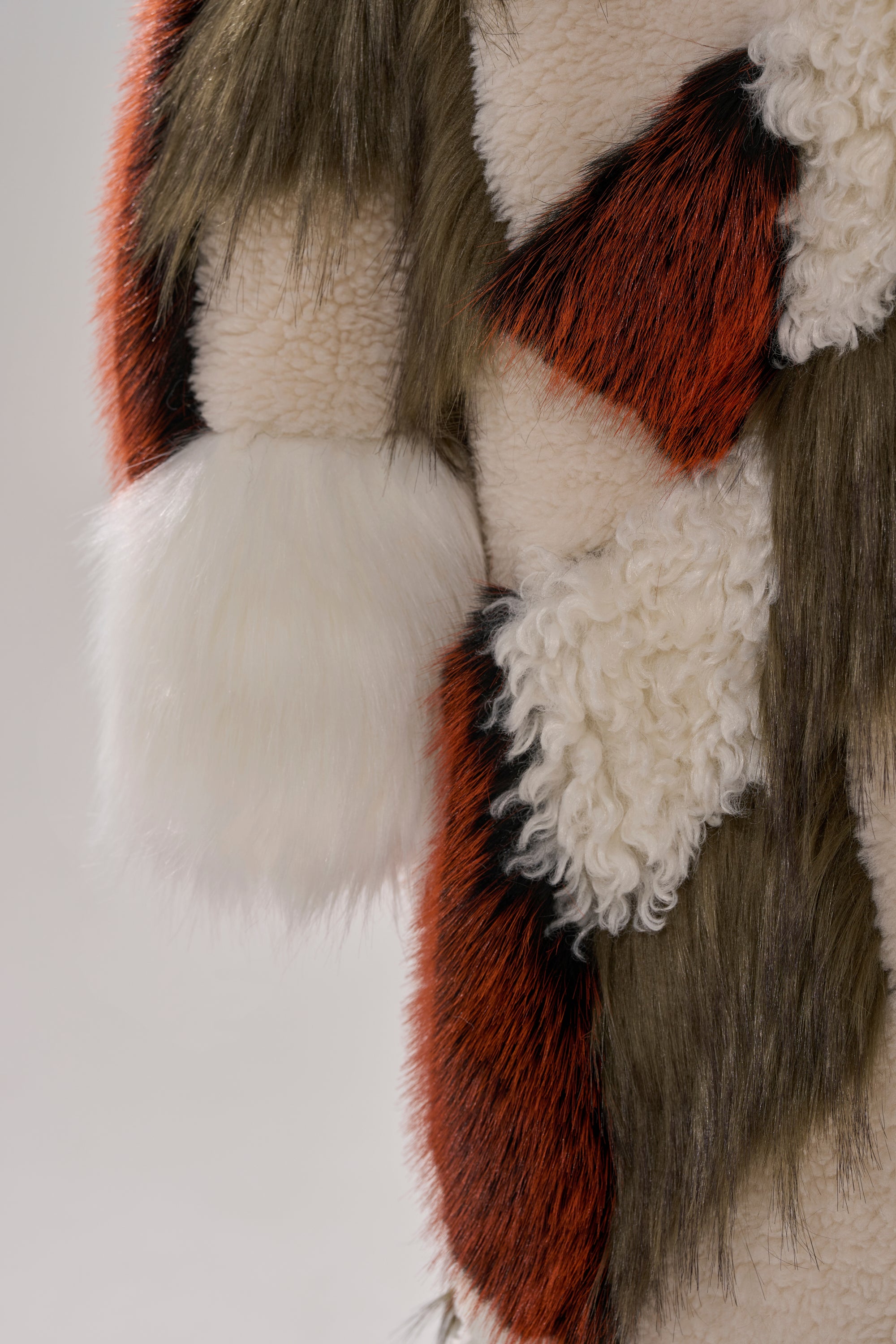 Close-up of FLEUR PATCHWORK FAUX FUR featuring textured fabric with curly cream wool patches and areas of long, straight brown, red, black, and white fur for a patterned, layered look.