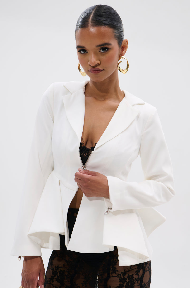 A woman with slicked-back hair and hoop earrings models the PARTY IN THE BACK FISHTAIL BLAZER with black lace pants and a matching bra, striking a confident pose against a white background.