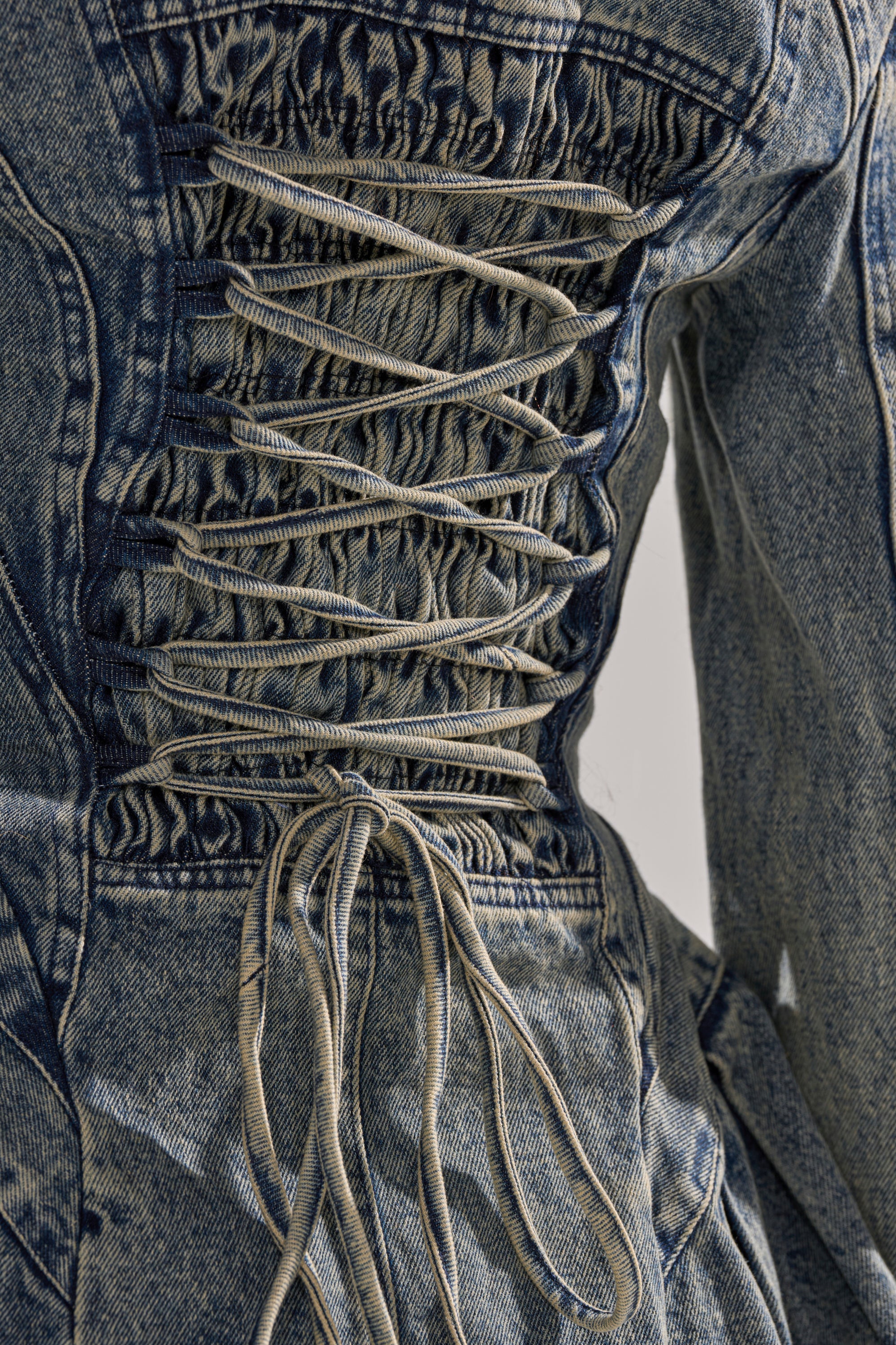 Close-up of the back of the Mallorca Peplum Denim Jacket with a corset-style lace-up design, crisscrossed denim ties, and gathered fabric for a structured, fitted look.
