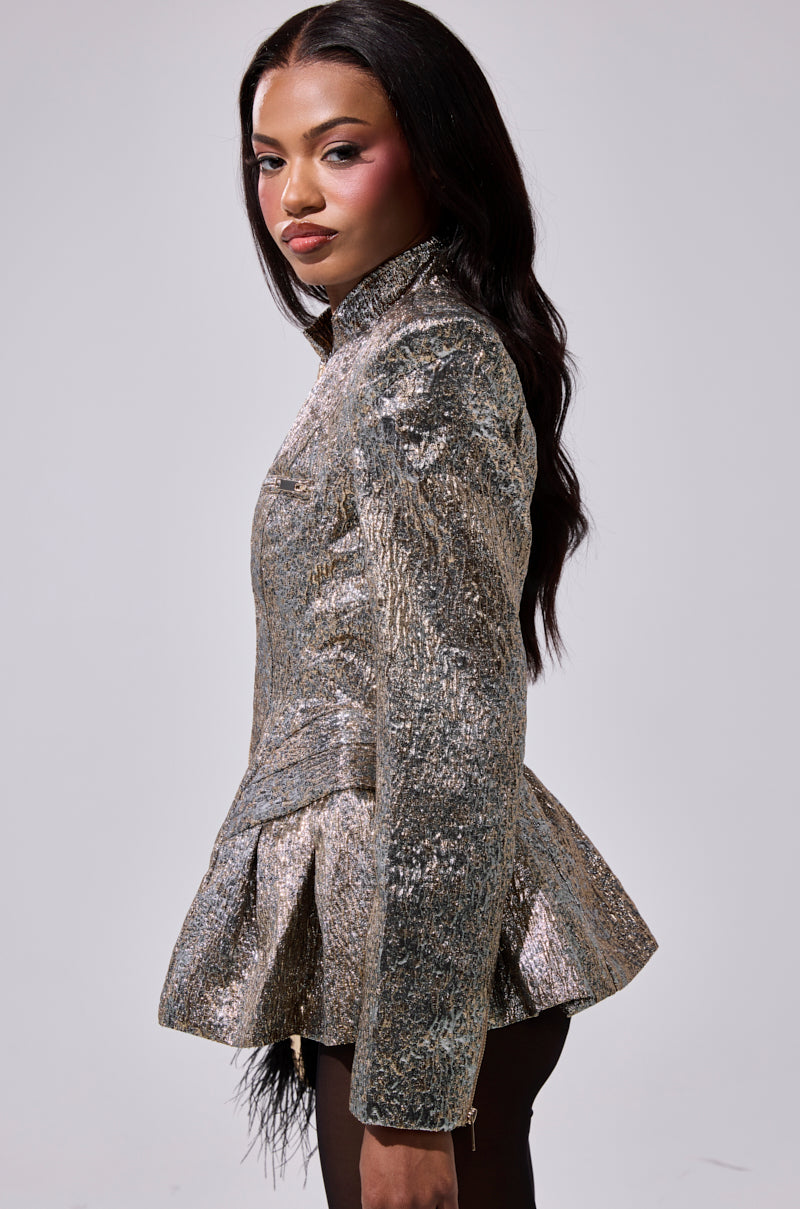 A woman with long dark hair poses in profile, wearing the BRONZE BROCADE BLAZER paired with black pants against a plain gray background.