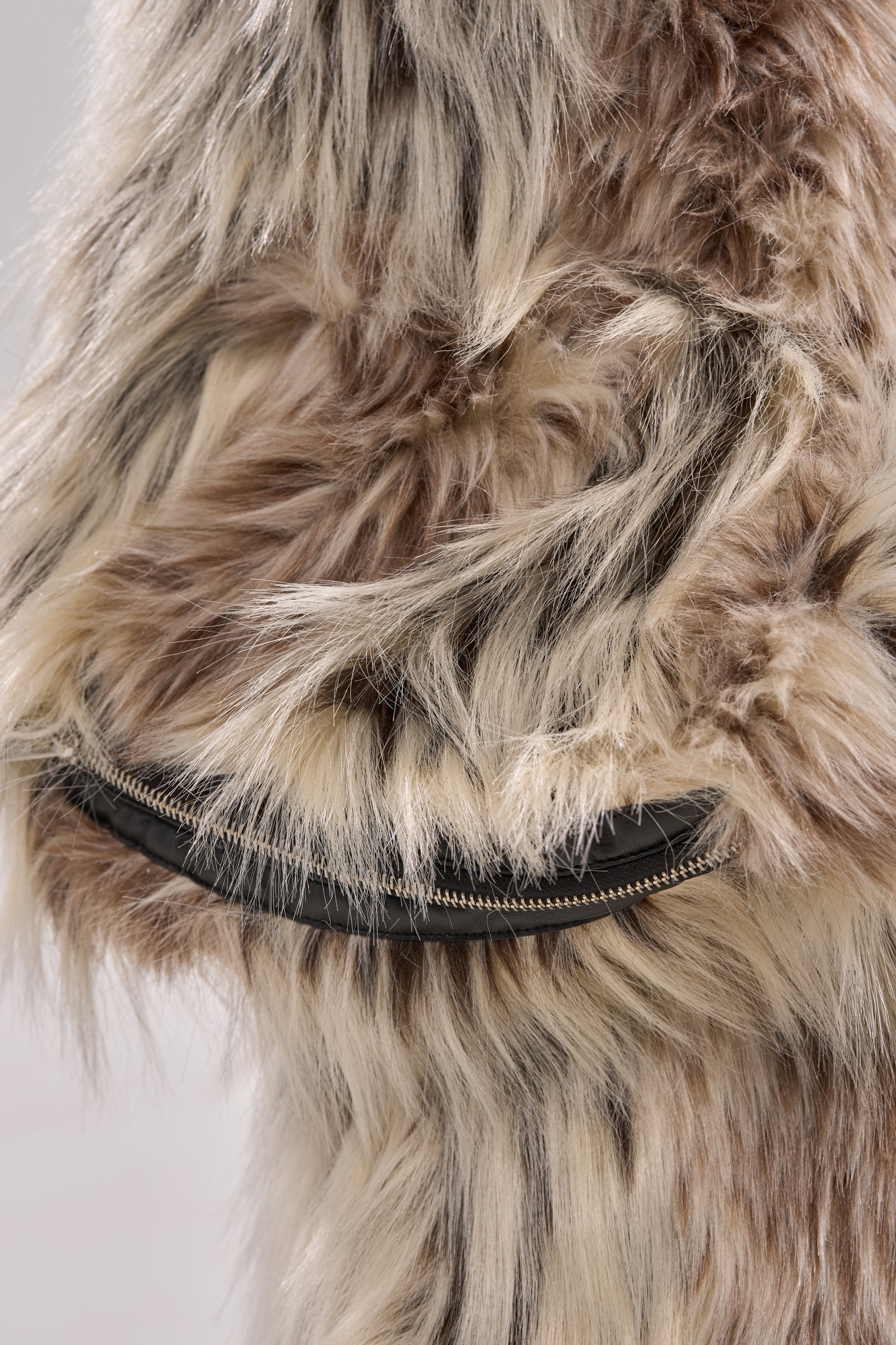 A close-up of the PARTICULAR TASTE FAUX FUR jacket, made from long, shaggy plush in beige, brown, and cream tones, with a visible black zipper partially embedded in the fur.