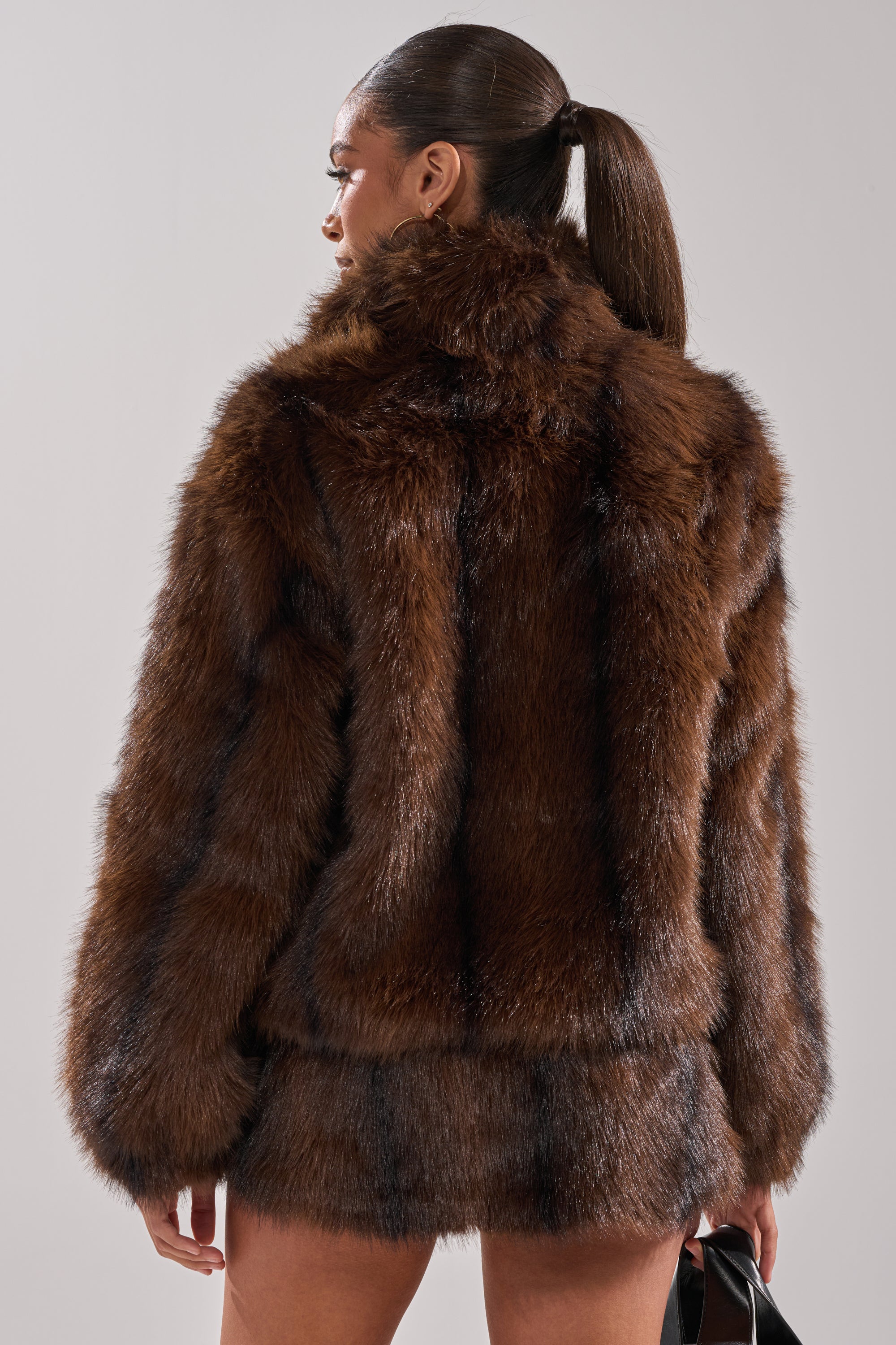 A woman with a sleek ponytail is shown from behind, wearing the COZY VIBES QUARTER ZIP FUR SWEATSHIRT and a matching mini skirt, exuding cozy style as she holds a small black handbag against a plain light background.