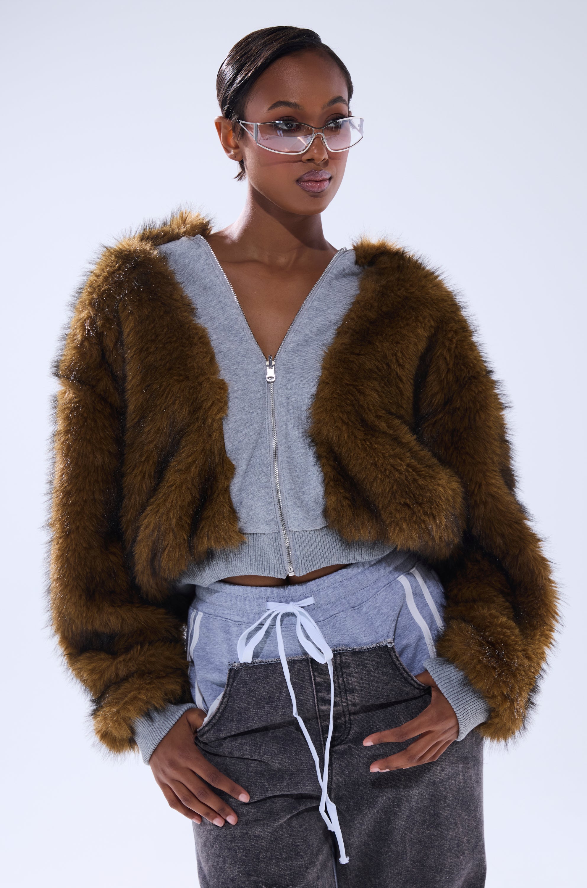 A person in clear glasses and dark pants with a white drawstring wears the BEST OF BOTH WORLDS REVERSIBLE FUR SWEATSHIRT over a gray zip-up top, standing confidently against a plain light background.