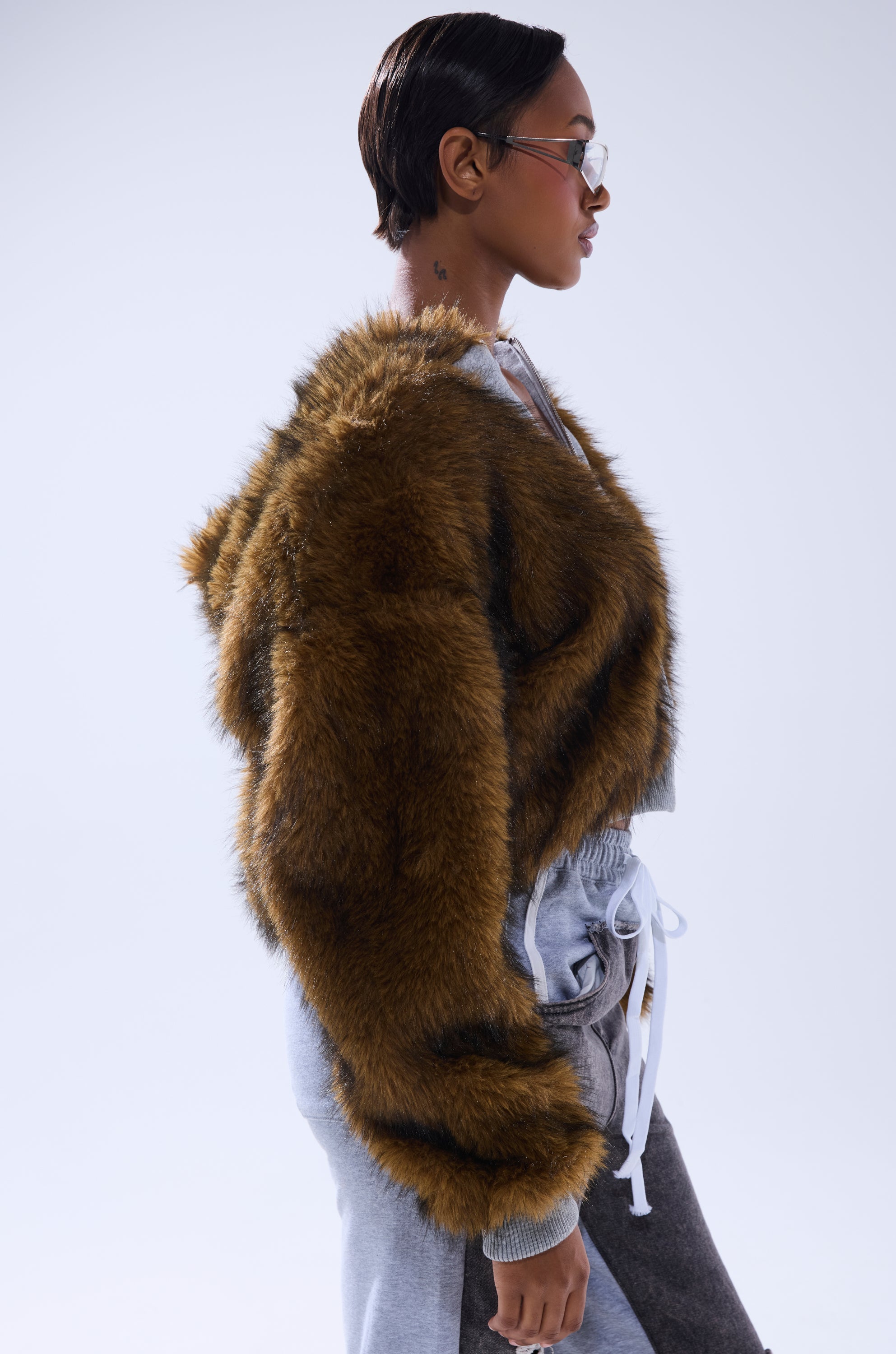 A woman in profile wears glasses, gray drawstring pants, and the BEST OF BOTH WORLDS REVERSIBLE FUR SWEATSHIRT, standing against a plain light background.