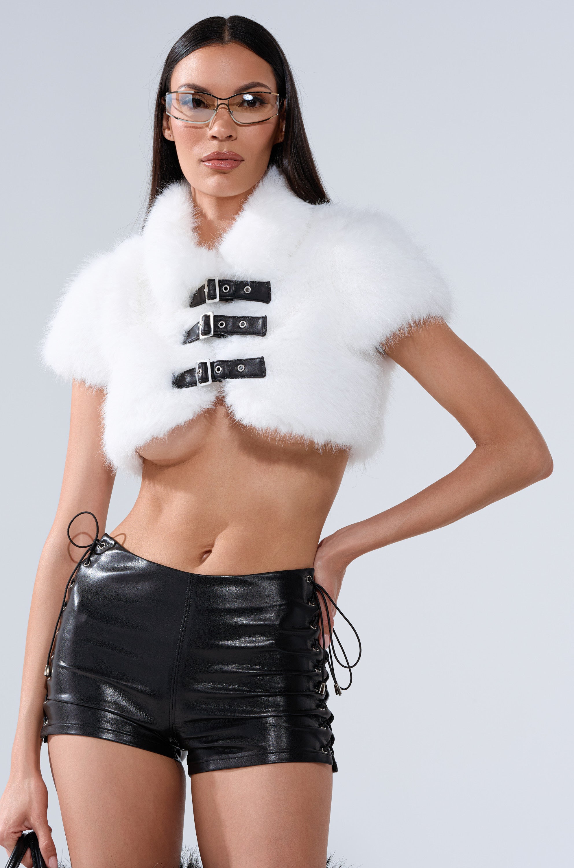 Wearing the SNOW WHITE CROP FUR SWEATER paired with high-waisted black leather shorts featuring lace-up sides and buckles, a person stands against a plain background. 0
