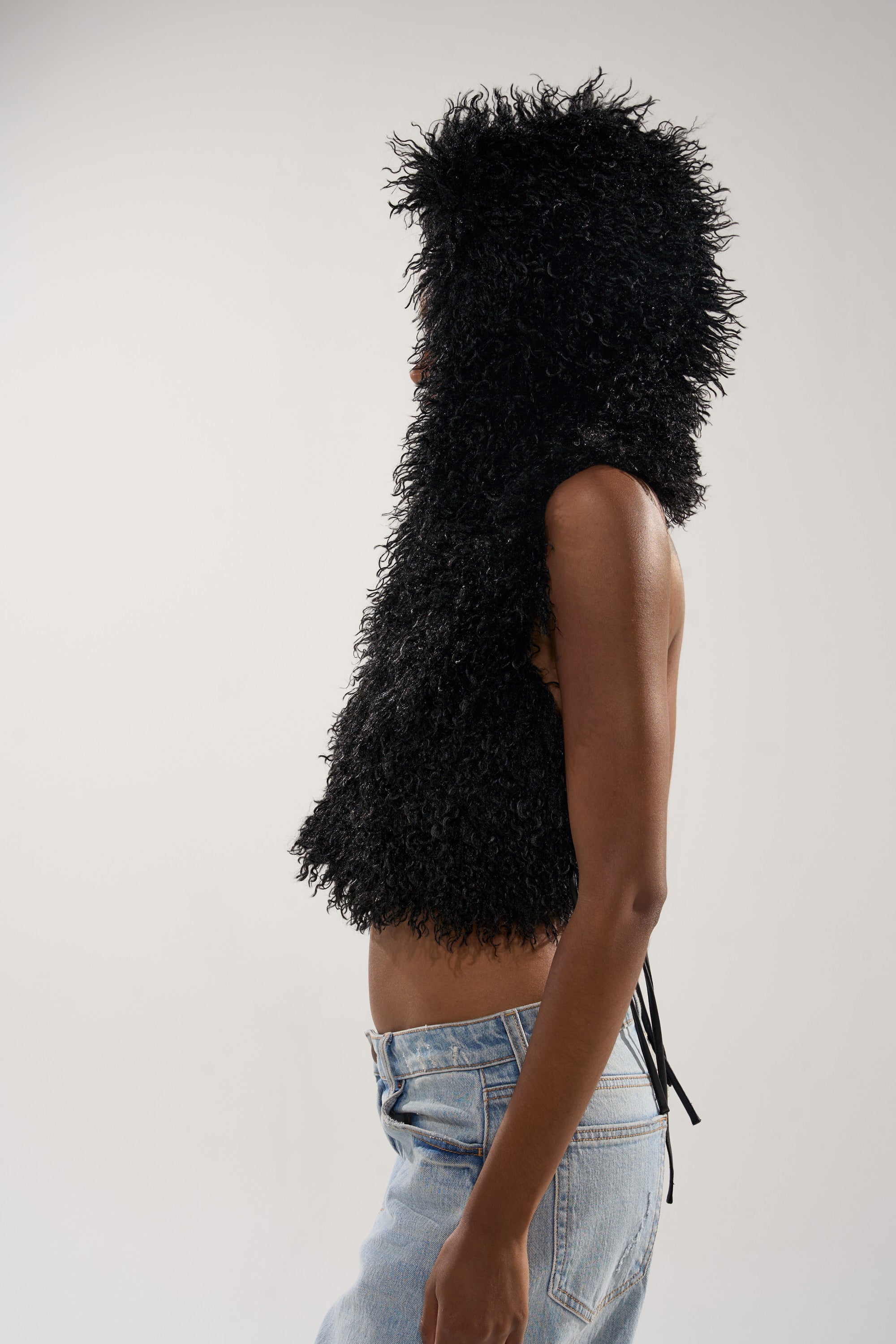 A person shown in profile against a plain light background wears the THINK ABOUT YOU ALL THE TIME FUR BLOUSE IN BLACK with light blue denim jeans.