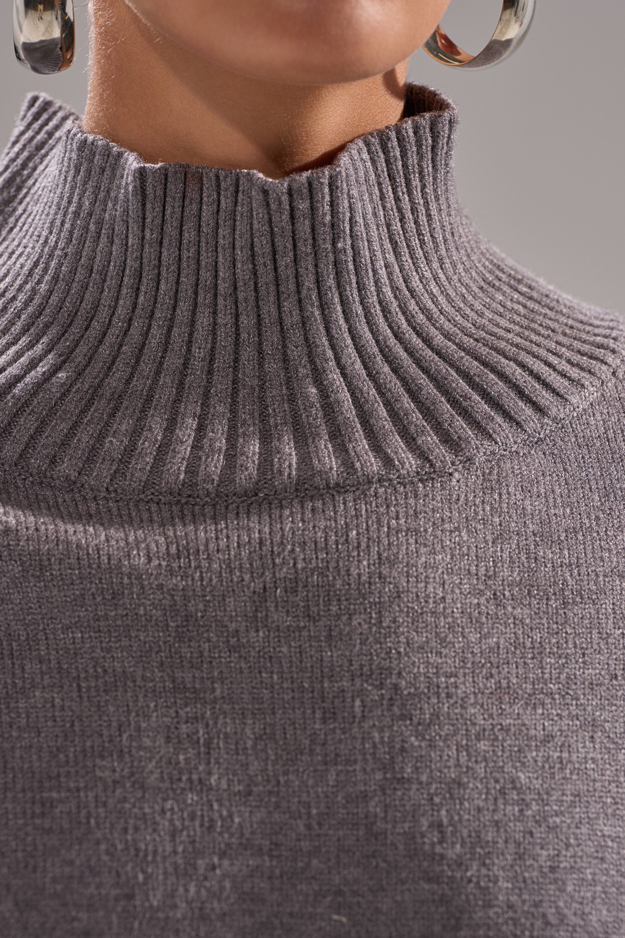 Close-up of a person wearing the TOUCH ME SWEATER WITH FUR CUFFS, featuring a ribbed gray turtleneck and large silver hoop earrings. Focus is on the cozy texture and stylish neckline of the sweater.