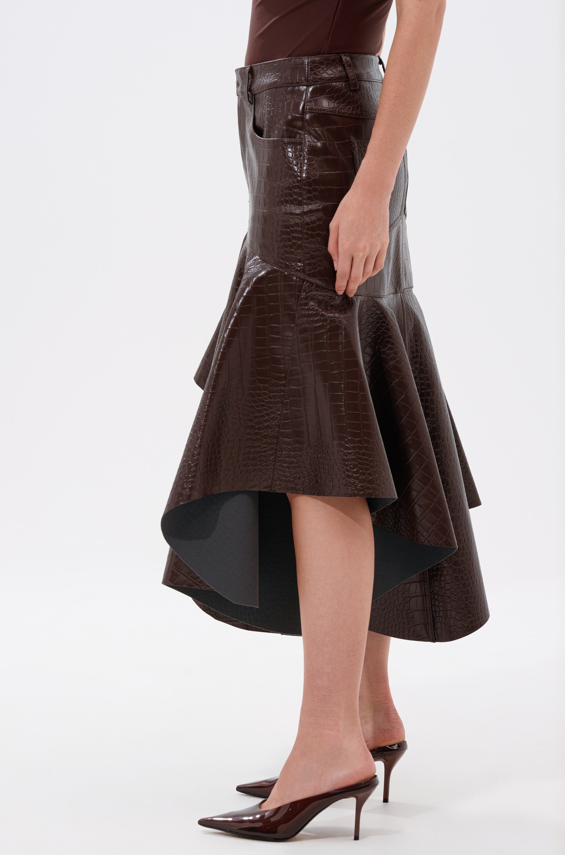 A person wears the RELAX WITH ME CROCODILE MIDI SKIRT featuring a high-waisted, asymmetric faux crocodile leather design with a flared hem, styled with a brown sleeveless top and pointed-toe heels against a plain white background.