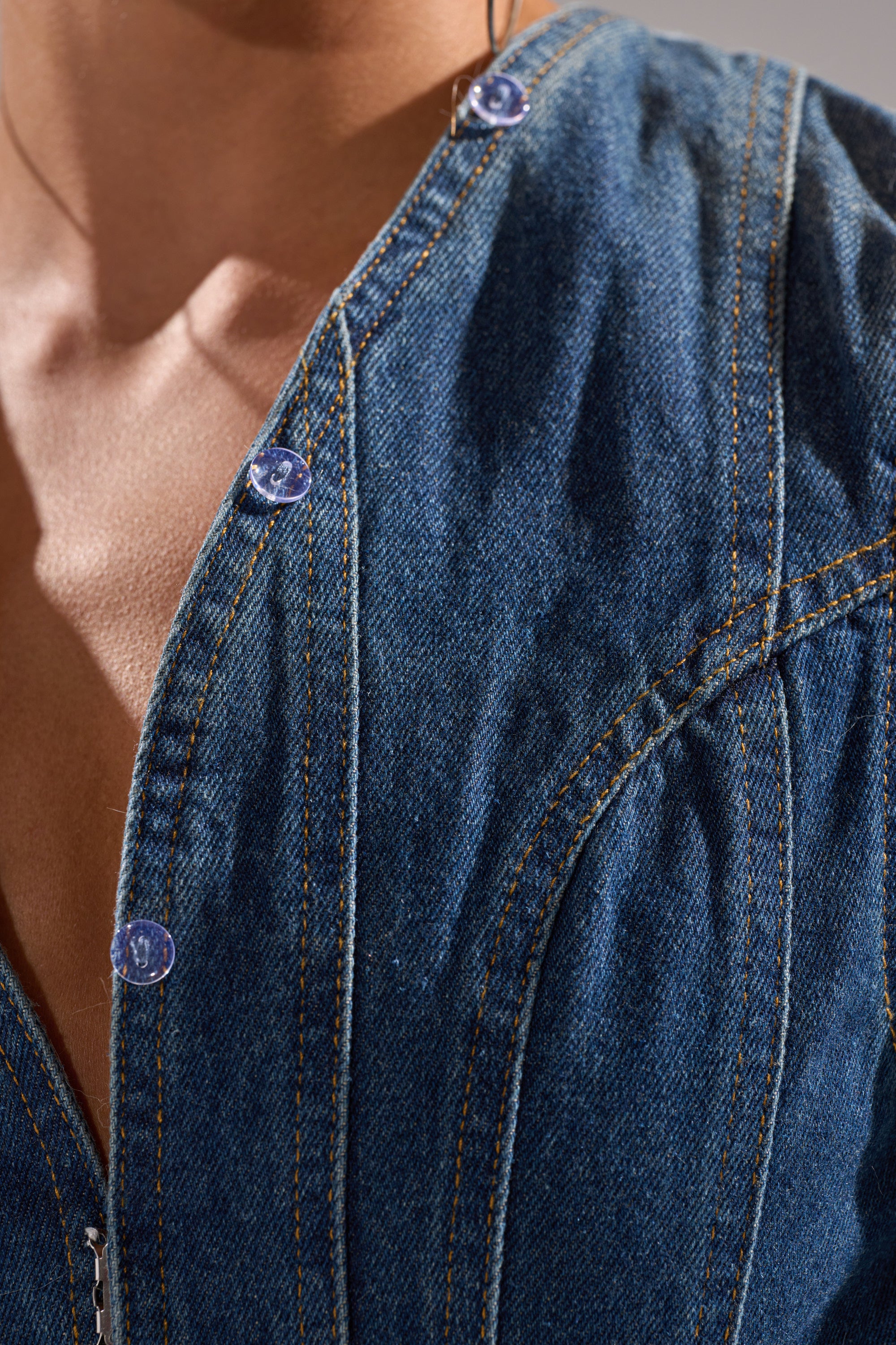 Close-up of a person wearing the LENNOX DENIM JUMPSUIT WITH FUR ACCENTS, featuring visible seams and silver buttons at the neckline, with lighting that highlights the texture of the denim and the person's skin.