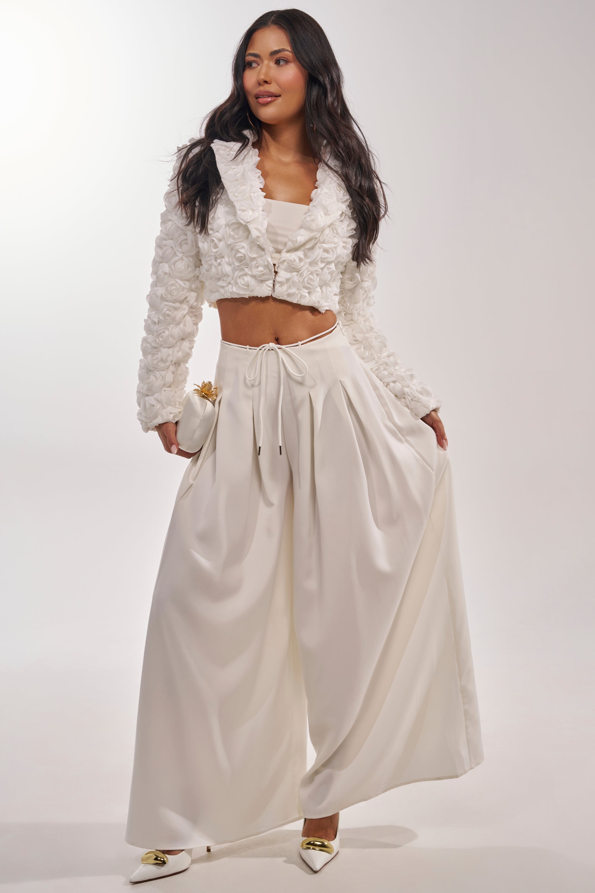 A woman poses in the FAYE FLORAL APPLIQUE BLAZER with wide-legged satin pants, a fitted top, and pointed white heels with gold detail, standing against a plain light background. 10