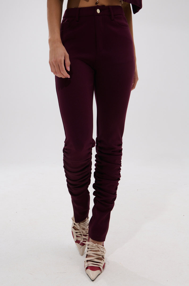 A person wearing the LYNX STACKED TROUSER IN BURGUNDY and pointed-toe, lace-up nude heels stands against a plain white background. 1