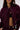 A woman wears the LYNX Layered Bomber Jacket in Burgundy, featuring gold zippers and buttons, partially unzipped to show a black crop top and high-waisted pants. Only her lower face is visible.