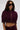 A woman wears the LYNX LAYERED BOMBER JACKET IN BURGUNDY, styled as a sleek two-piece set with oversized black sunglasses, standing against a plain light background.