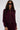 A woman with long dark hair wears large black sunglasses and the LYNX LAYERED BOMBER JACKET IN BURGUNDY, paired with matching pants, standing against a plain light background.