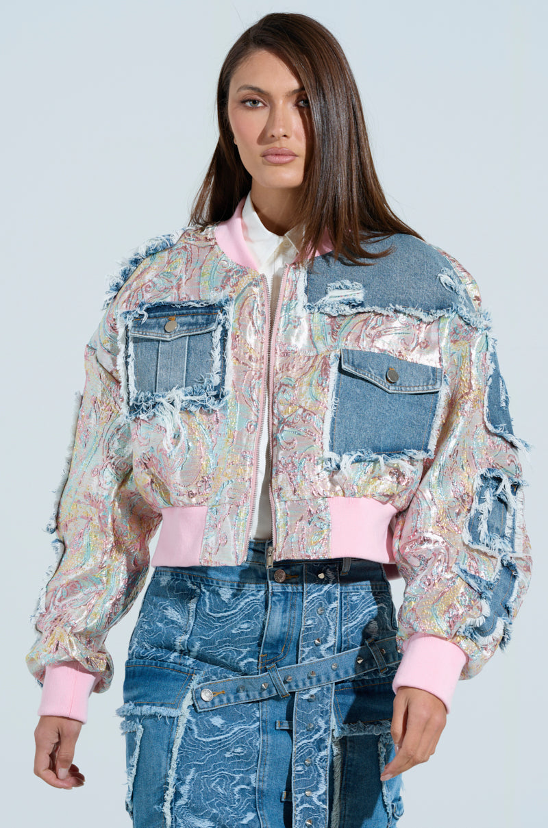 A person wearing the SPRING REFRESH BROCADE BOMBER with matching skirt embodies a Pastel Daydream vibe. The bomber showcases colorful patchwork, frayed edges, varied textures and patterns with pink accents, all set against a light-hued background enhancing its allure.