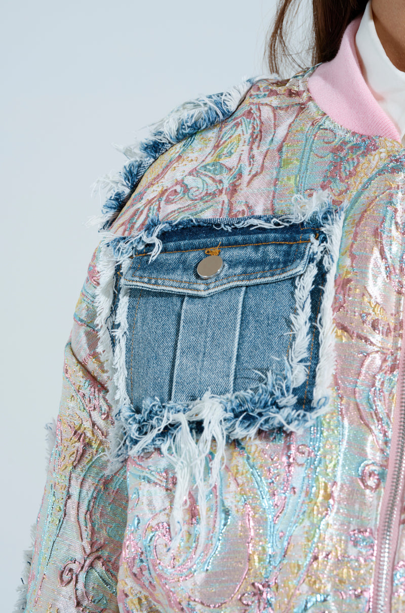 Close-up of the SPRING REFRESH BROCADE BOMBER, showcasing a vibrant metallic paisley pattern with a frayed denim pocket featuring button closure on the sleeve and a collar in soft pastel daydream pink.