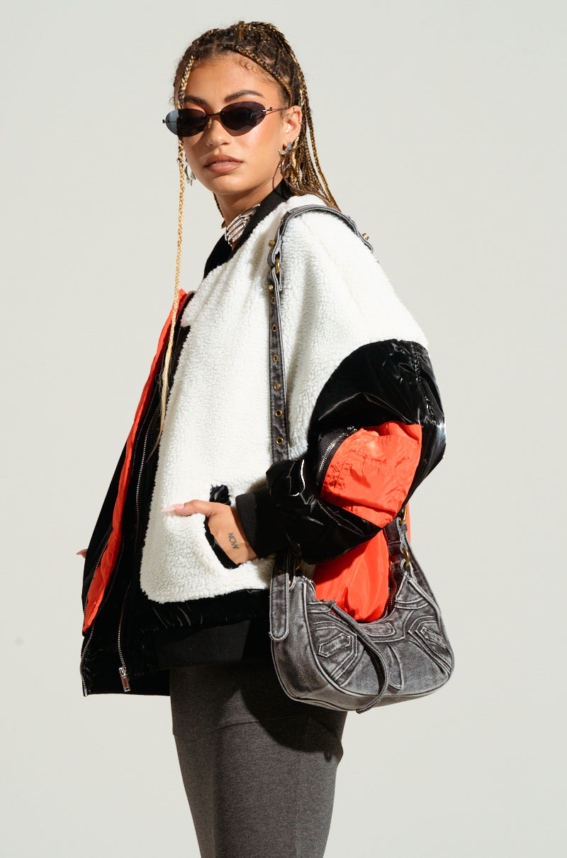 A person with braided hair and sunglasses dons a sleek Urban Chic Ensemble, showcasing a white and black jacket with orange lining in the style of the LENNIE MIXED MEDIA BOMBER, while holding a gray handbag. They stand confidently against a plain background.