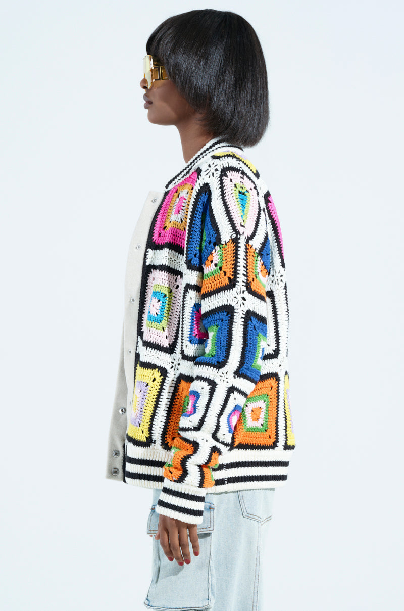 A person wearing gold sunglasses and the ALHAMBRA CROCHET BOMBER stands in profile against a plain background, pairing it effortlessly with light blue jeans.