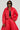 Dressed in the VIVI Cropped Puffer Bomber in Red, an individual showcases a striking look with matching wide-leg pants, complemented by a black top and sunglasses. The outfit is accessorized with a chunky chain necklace and set against a simple light gray background.