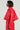 A person with short hair and large, reflective sunglasses stands in profile against a plain off-white background, wearing the VIVI CROPPED PUFFER BOMBER IN RED from the AKIRA Label Vivi collection.